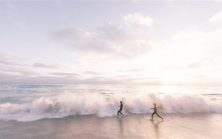 two person running on seaside beach during daytime MacBook Pro wallpaper