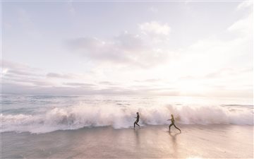 two person running on seaside beach during daytime MacBook Pro wallpaper