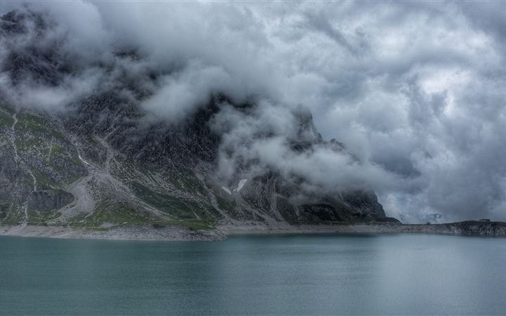 body of water beside mountain covered with fog All Mac wallpaper