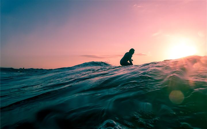 man surfing on ocean water during golden hour MacBook Pro wallpaper