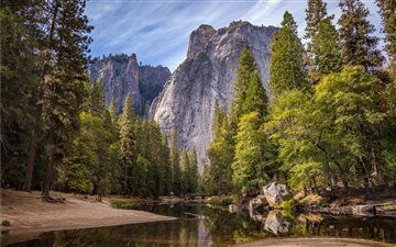calm body of water surrounded by trees near cliff All Mac wallpaper